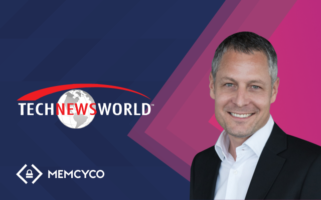 A man in a business suit smiles at the camera next to the Tech News World logo and a Memcyco logo, highlighting solutions against website impersonation on a blue and pink geometric background.